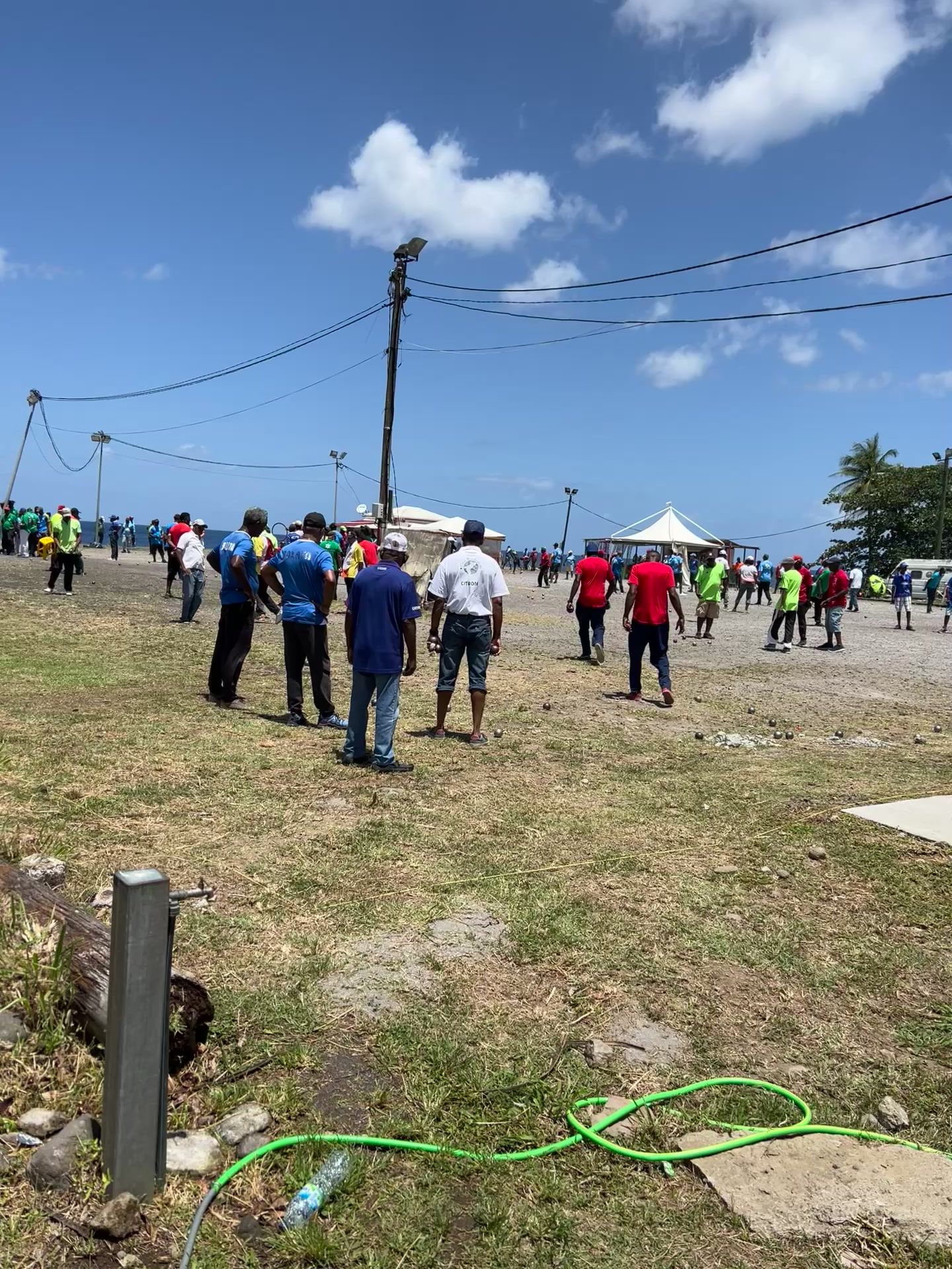 Concours de pétanque en bord de mer en Martinique : des dizaines de joueurs en maillots de club sur un terrain en terre, sous un grand ciel bleu